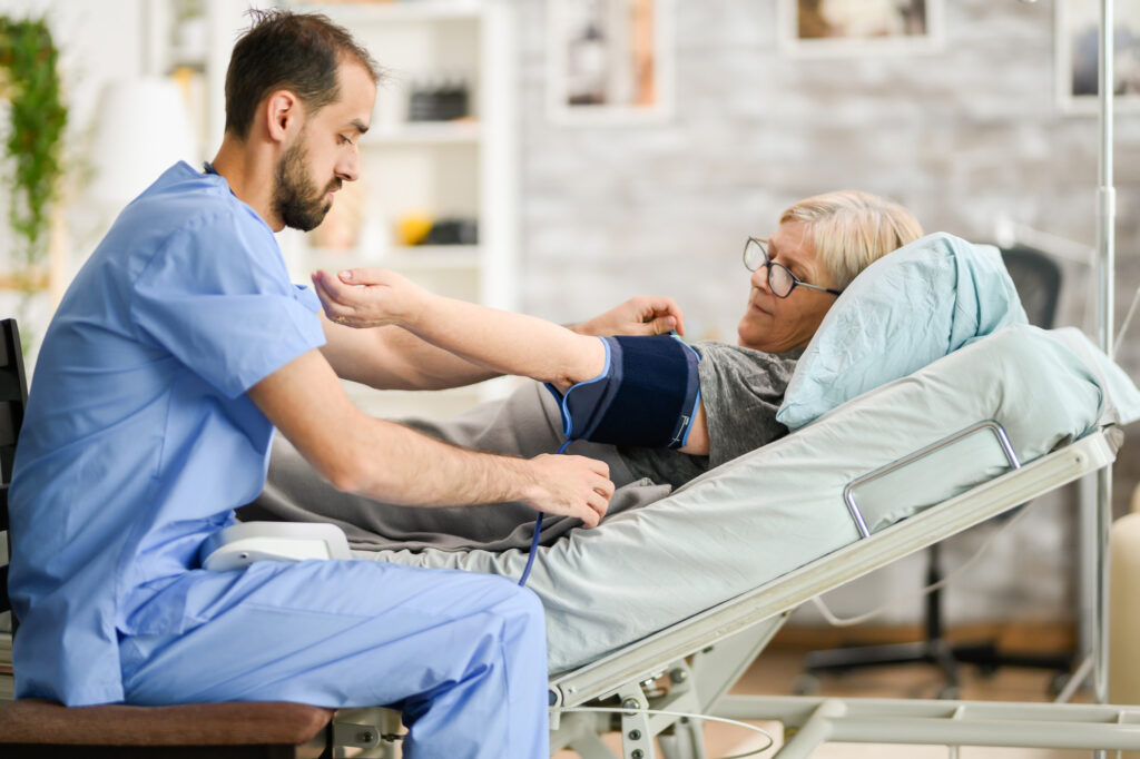 Pfleger misst einer älteren Patientin im Pflegebett den Blutdruck
