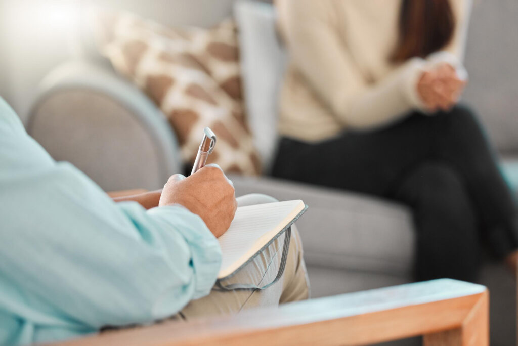 Psychotherapeut mit Notizblock im Gespräch mit einer Patientin auf dem Sofa